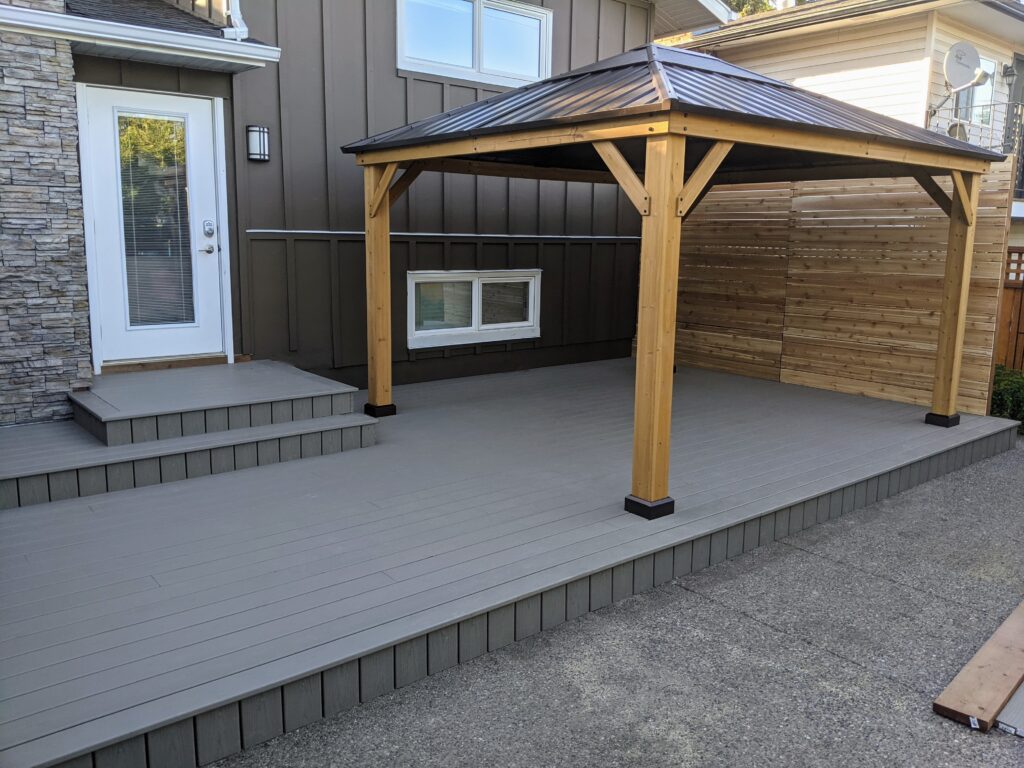Modern wooden gazebo on a gray deck with steps and a door.