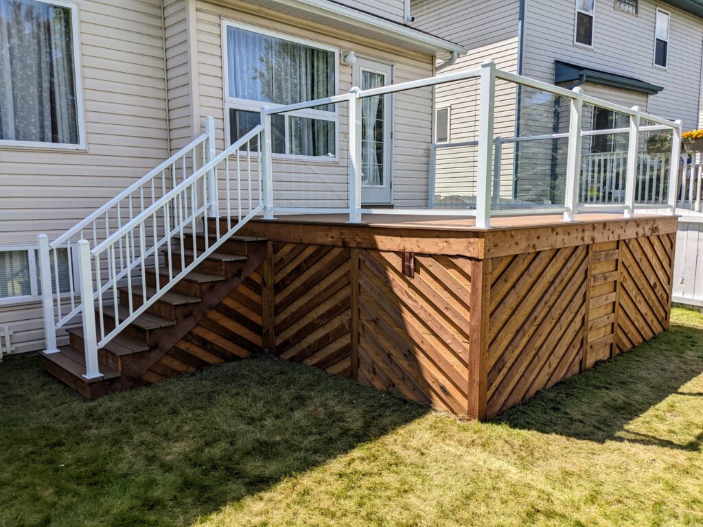 A wooden deck with diagonal paneling and glass railing on a house.