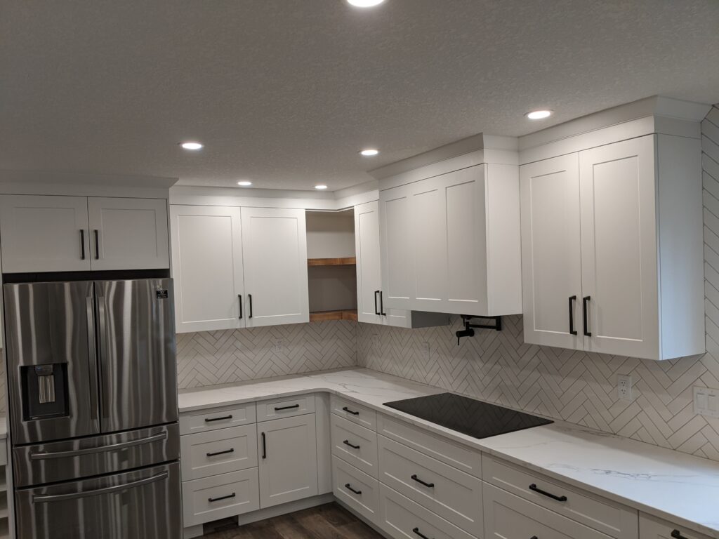 Modern white kitchen with stainless steel fridge and ample cabinetry.