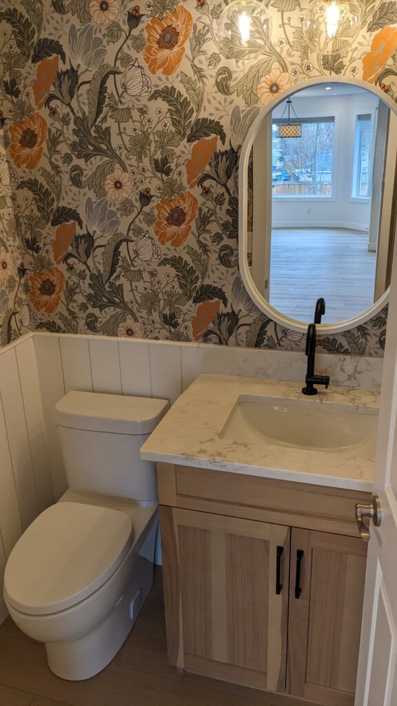 Bathroom with floral wallpaper and round mirror.
